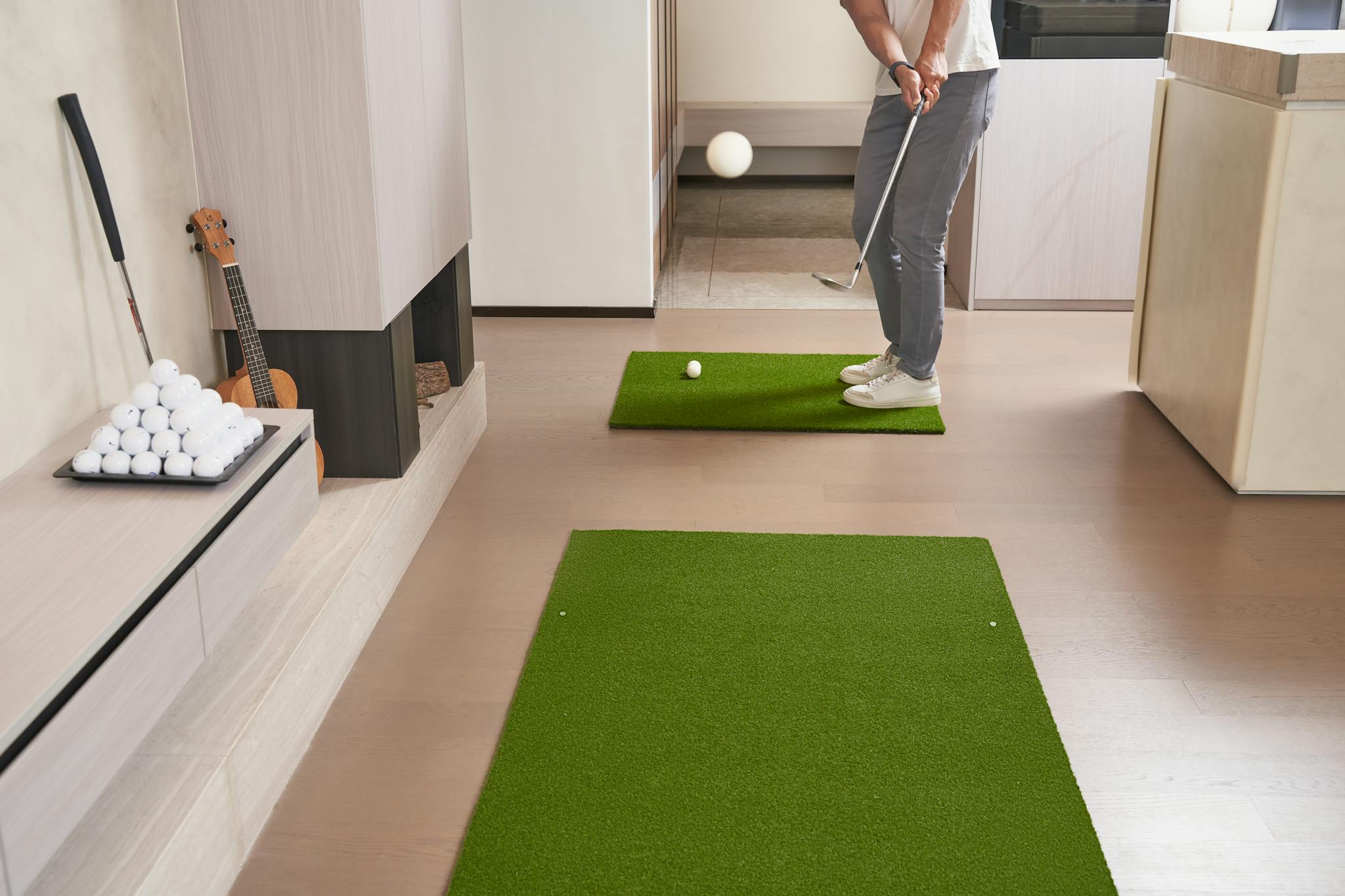 A golfer practicing putting indoors on artificial turf with a golf club and ball.