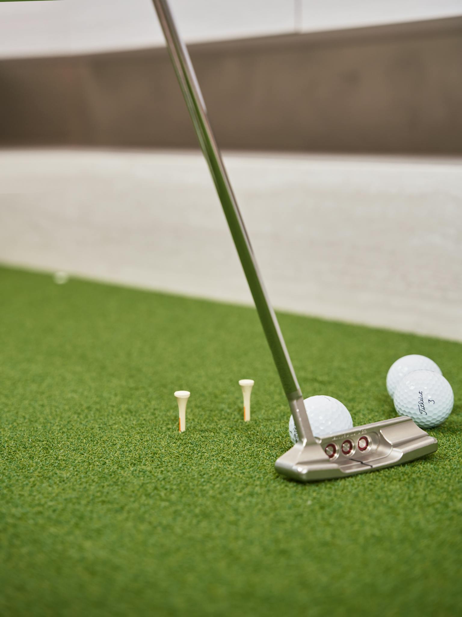 Focused shot of a golf putter with balls and tees on artificial turf.