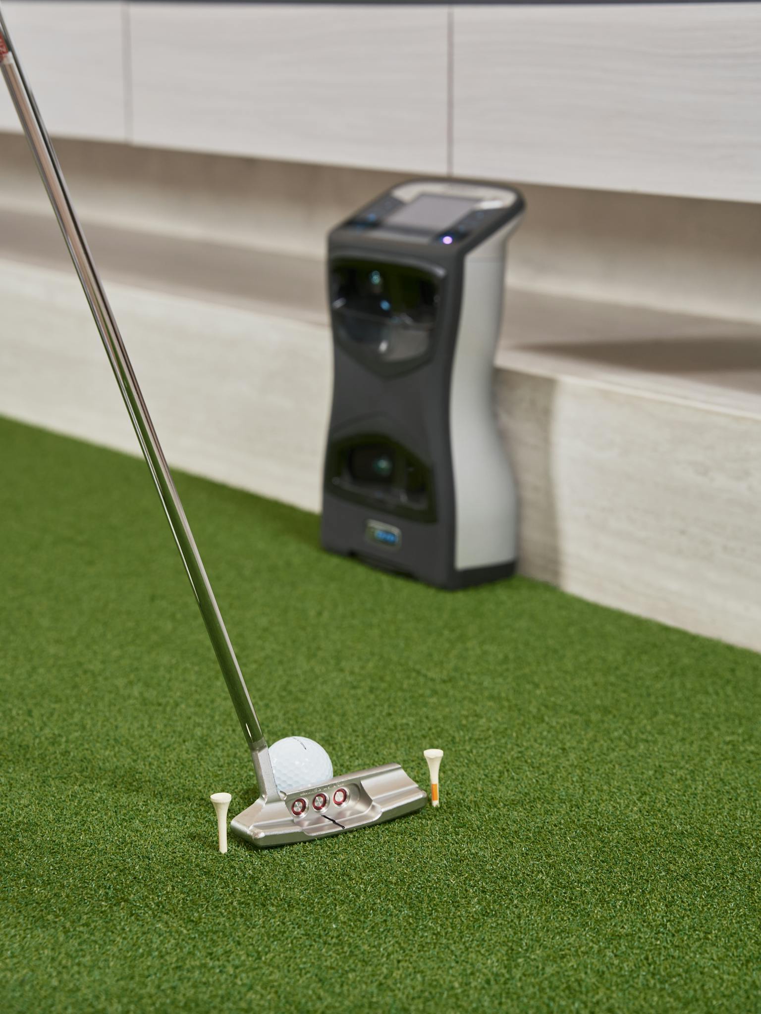 Indoor setup for practicing golf putting with a high-tech sensor and putter on artificial turf.